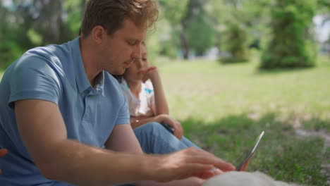 Aktive-Familie-Spielt-Mit-Labrador,-Der-Ein-Tablet-Auf-Dem-Rasen-Hält.-Vater-Streichelt-Labrador.