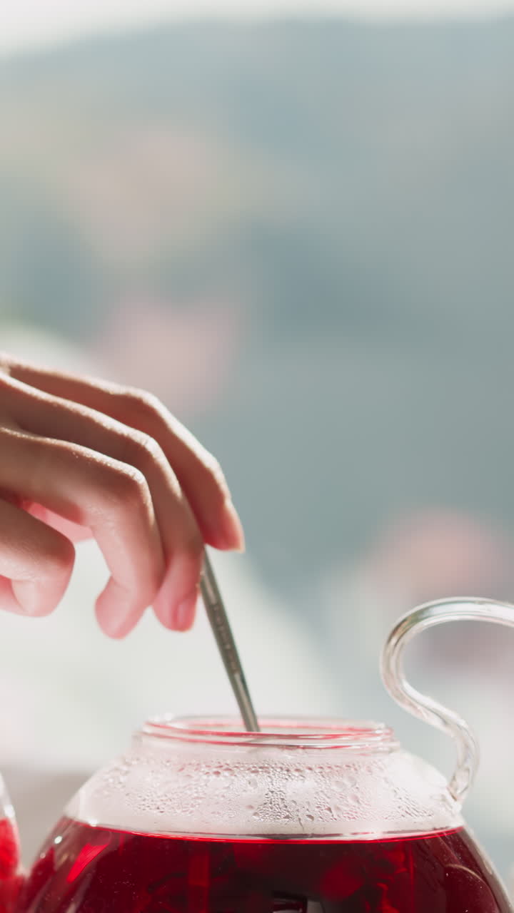 테이블 근처에 앉아 차 비에서 차를 는 여인. 욕조를 입은 편안한 여성이 창문 에 앉은 뜨거운 히비스쿠스 차를 술에 마시고 있습니다. 주말 아침의 개념