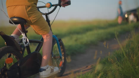 a young boy, dressed in yellow, rides his bicycle through a grassy field at sunset. vibrant red, blue, and yellow balloons are tied to the back of his bike. the boy's face is not visible