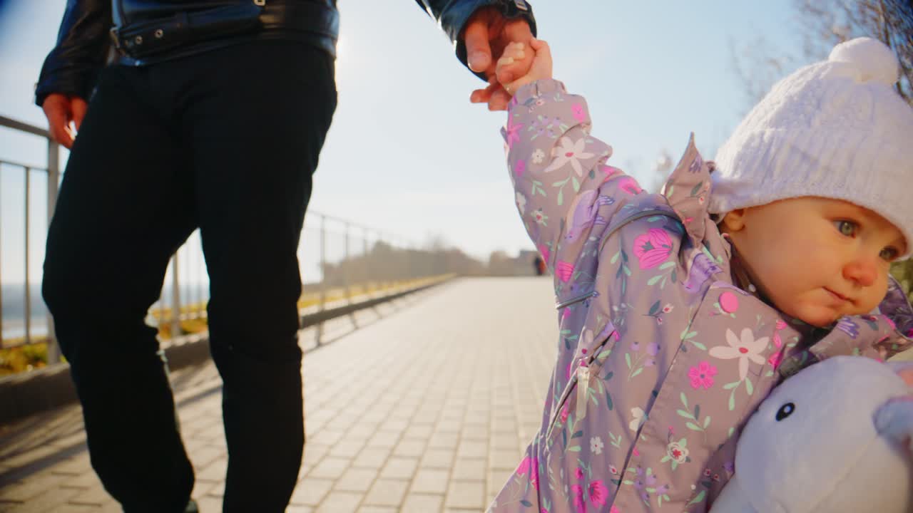 A Child's Joyful Day Out: Holding Hands with a Parent While Carrying a Stuffed Bunny in a Sunny Park Setting, Showing Innocence and Connection