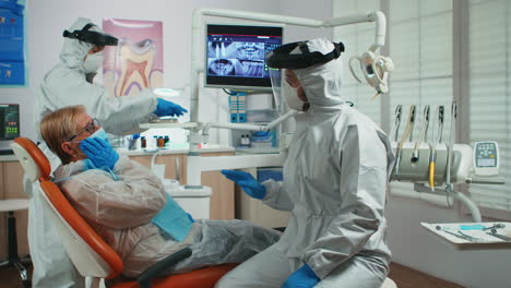 senior woman showing aching tooth to dentist dressed in coverall