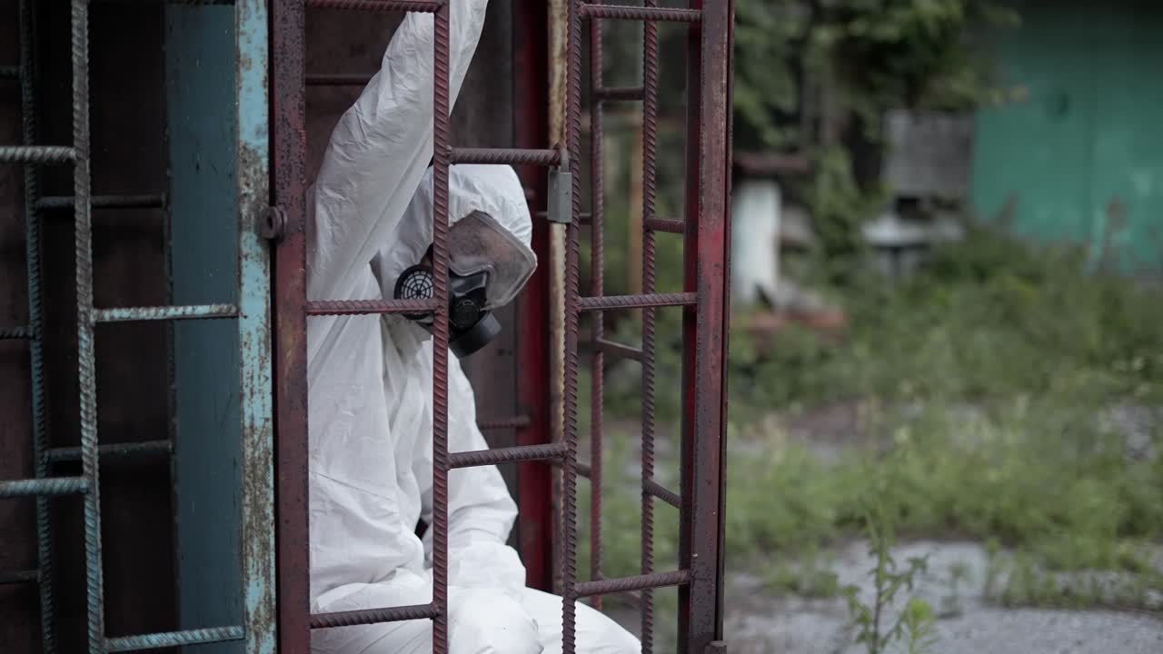 보호복을 입은 남자가 건물의 폐허에 앉아 장소를 탐험하고 주위를 둘러보고 있습니다.