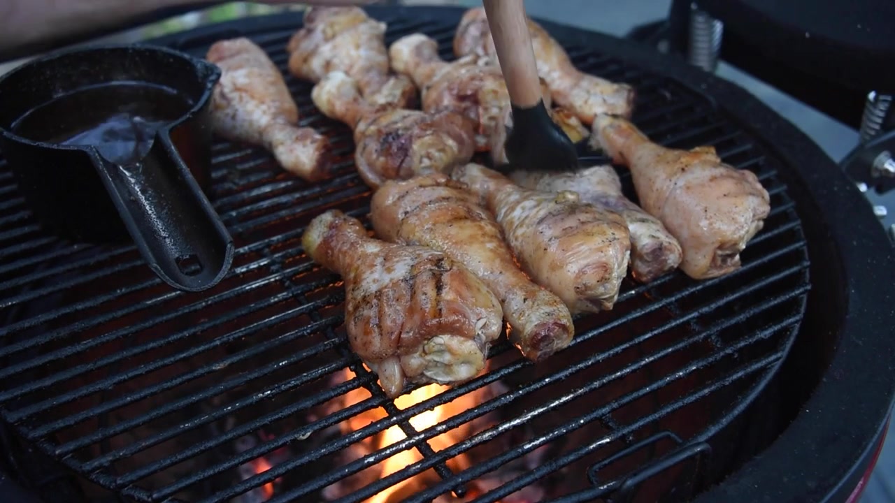 Deliziose cosce di pollo cuociono su una griglia a carbone ardente. Uno chef spennella il pollame condito con salsa barbecue per un pasto delizioso.