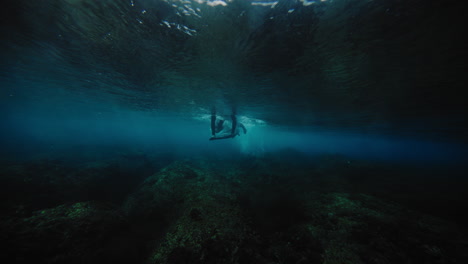 surfer paddles over shallow reef as they push down on board under crashing wave