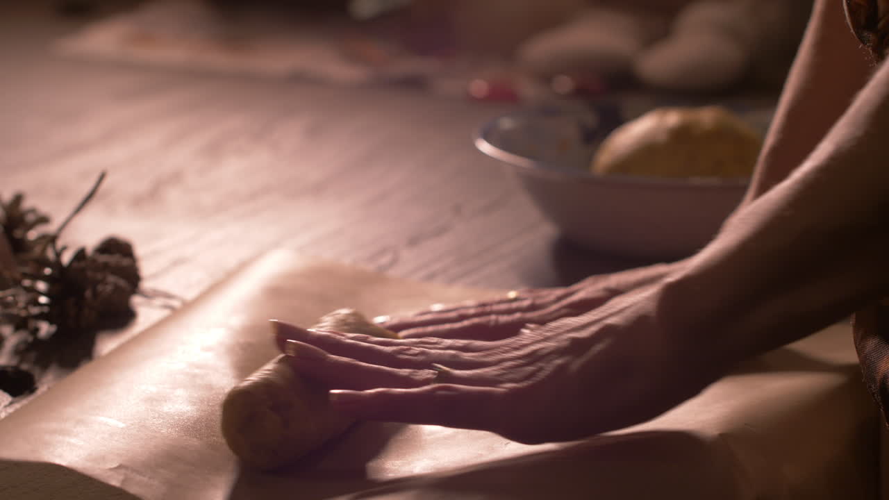 Woman baker rolling out raw dough on baking sheet in kitchen, close up on hands