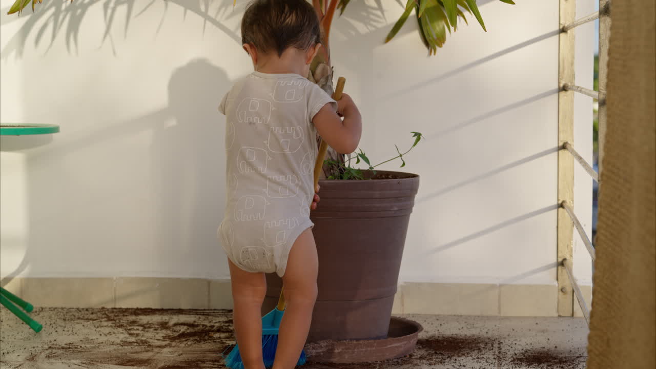 Little young latin toddler in a baby romper sweeping with a toy broom the dirt from the floor after a mischief