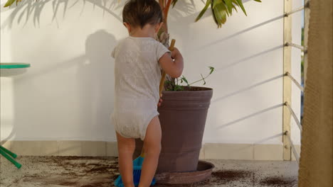 little young latin toddler in a baby romper sweeping with a toy broom the dirt from the floor after a mischief