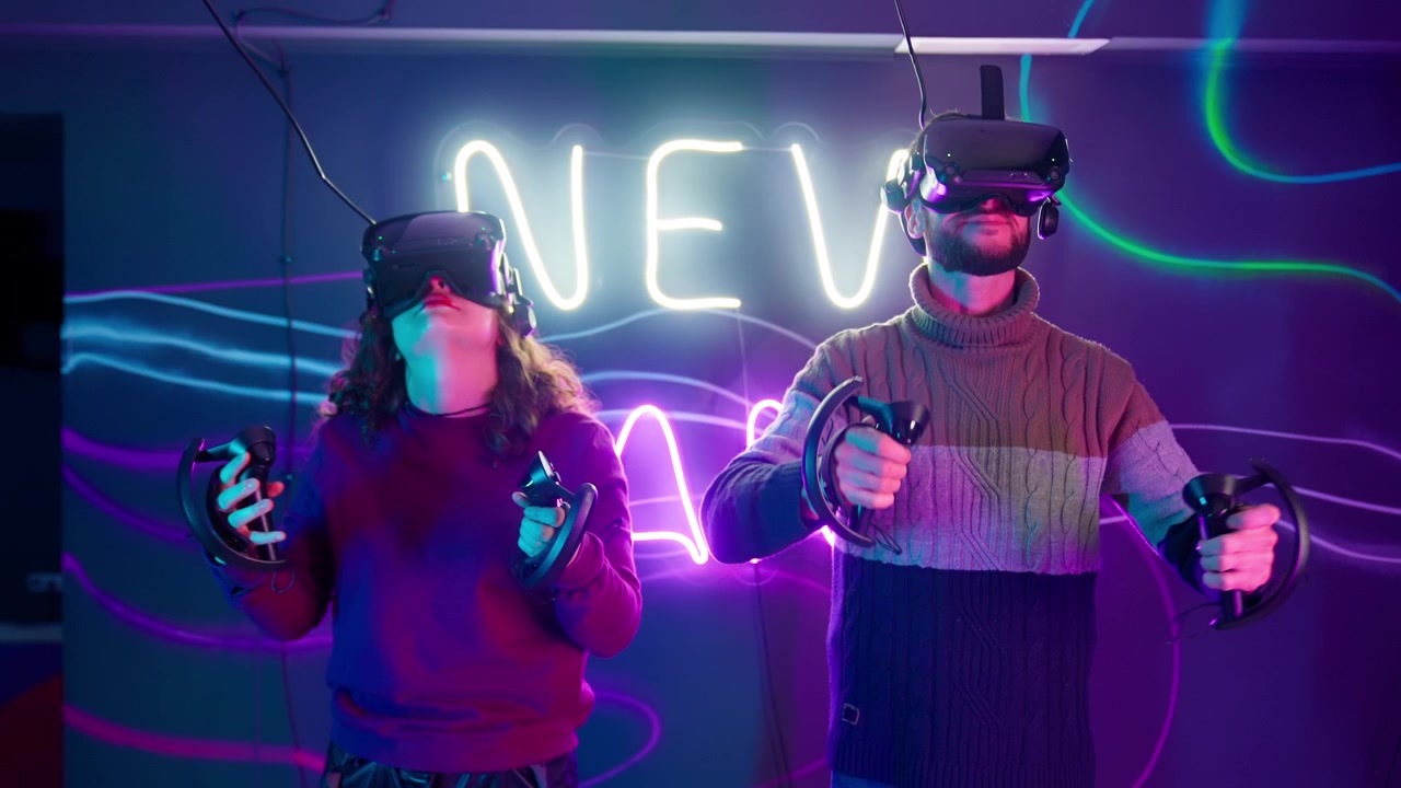 Pariskunta pukee virtuaalitodellisuuslasit ja ohjaimet neonvaloin valaistussa huoneessa