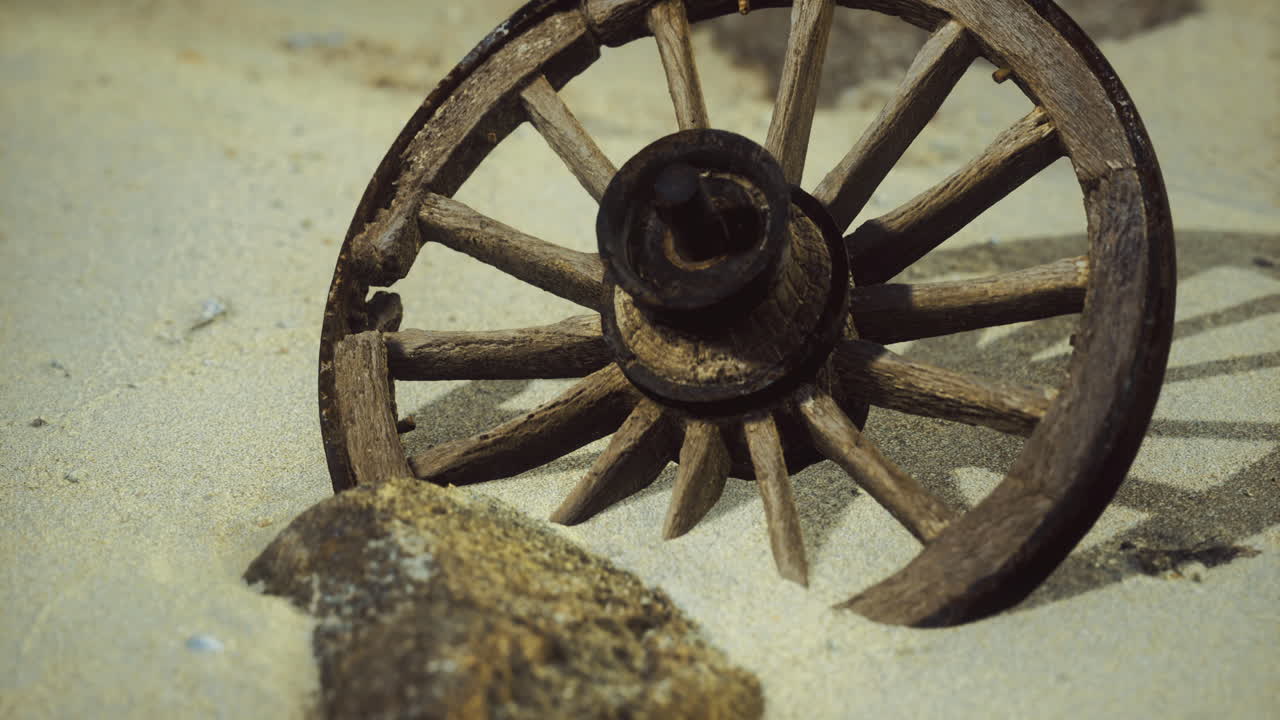 Wooden wagon wheel rests on sandy beach near stone