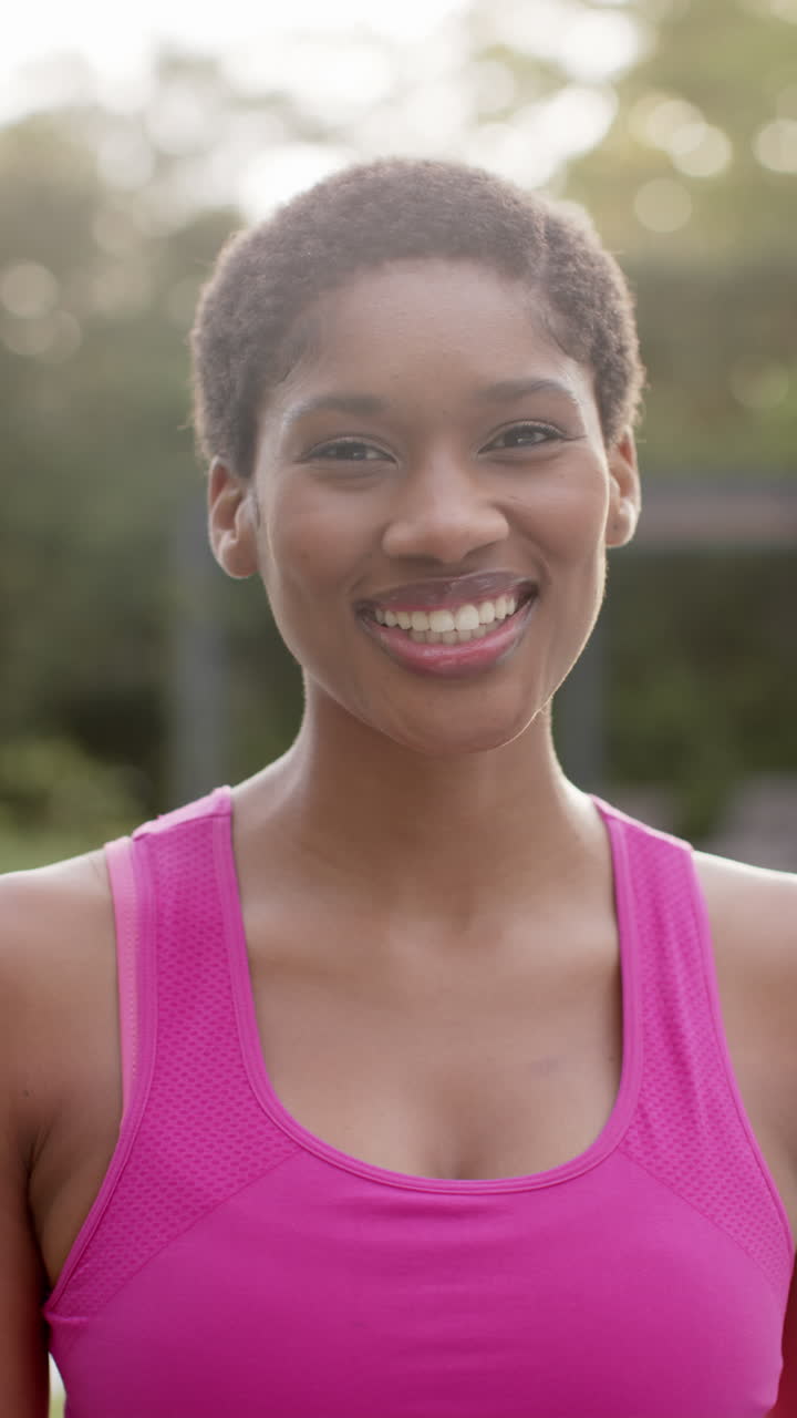 Retrato em vídeo vertical de mulher afro-americana feliz sorrindo no jardim, em câmera lenta.