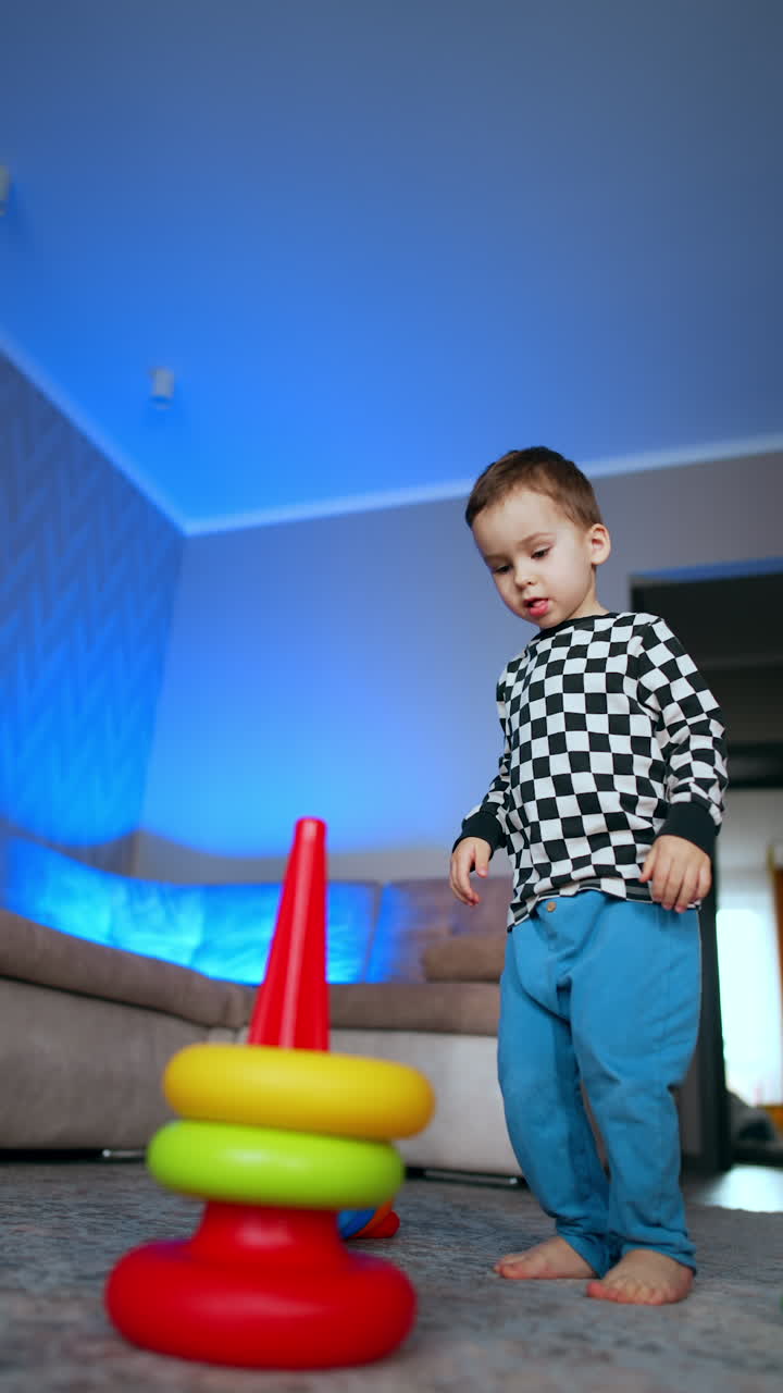 Cute baby boy assembling the pyramid in his room. Little kid playing cheerfully at home. Low angle view. Vertical video.