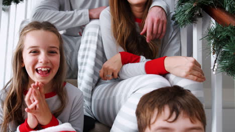 portrait of excited family wearing pajamas sitting on stairs on christmas morning