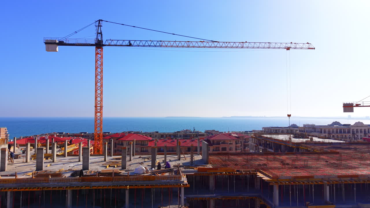 A yellow tower crane stands over a concrete reinforced residential building under construction near the sea coast during daytime