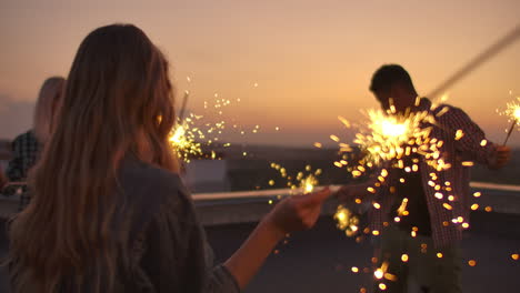compañía joven de personas en el techo se mueven un baile en una noche de verano con gran luz de bengala. es un atardecer de placer antes de la noche.