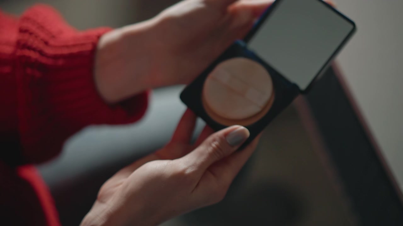 Close view of hands dipping fingertip into cream jar, smoothing product over skin, then lifting compact mirror for self-checking in warm indoor light with soft, calm home beauty routine