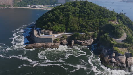 imagens aéreas girando em torno do museu histórico da fortaleza de são joão, no rio de janeiro, com ondas do oceano batendo contra as rochas