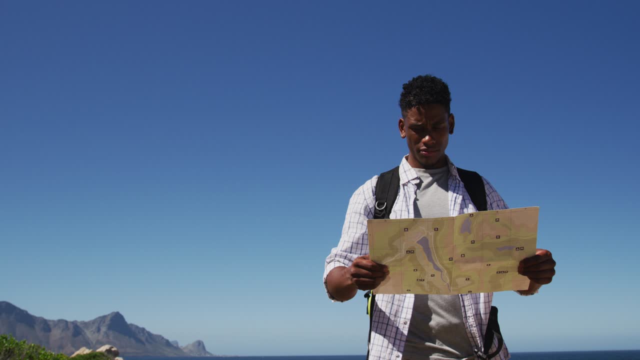 Afroamerikansk mand, der vandrer og læser et kort i et kystlandskab.