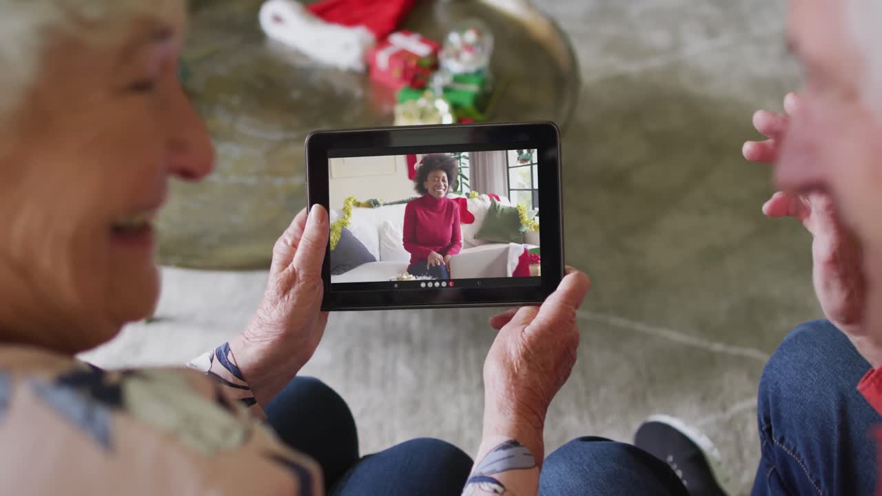 Coppia anziana caucasica sorridente che usa un tablet per una videochiamata di Natale con una donna sullo schermo