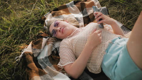 lady in net cloth and sunglasses lying on mat with warm smile conversing with someone in background, relaxed countryside setting, soft natural light, peaceful atmosphere