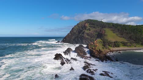 aerial view of ocean waves hitting rocky cliffs under clear skies at byron bay, australia. captures dynamic movement and natural beauty