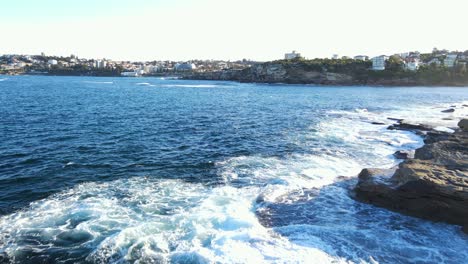 Olas-Del-Océano-En-La-Costa-Rocosa-De-La-Bahía-Clovelly-Con-Vistas-A-Los-Suburbios-Del-Este-De-Sydney,-Australia