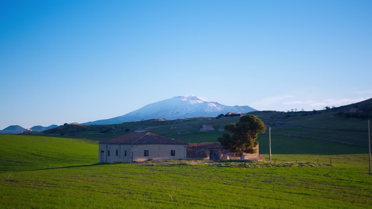 спокойный вид на дом, расположенный на склоне горы этна, с огромным зеленым полем на рассвете в сицилии