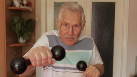 anciano caucásico haciendo ejercicios deportivos con pesas en casa