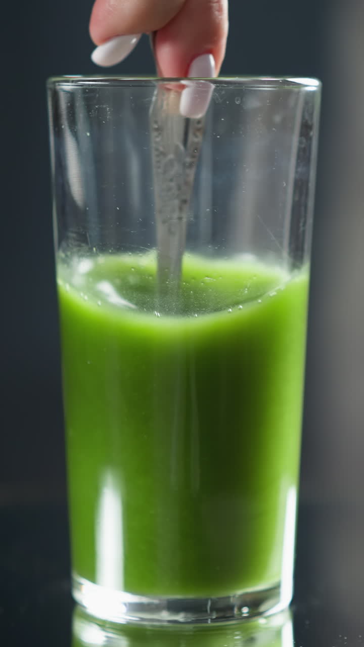 cuchara agitando jugo de verduras de color verde brillante en un vaso transparente con un fondo borroso