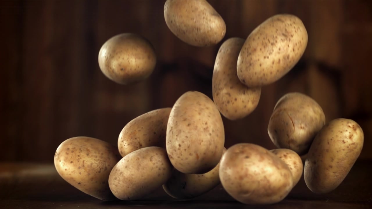 Patate fresche e crude che cadono su una superficie di legno scuro al rallentatore.