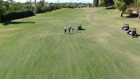 Golfers-standing-around-chatting-while-their-friend-gears-up-for-a-swing