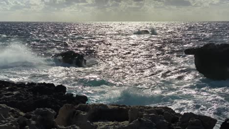 sunlight reflects off blue ocean crashing against backlit rocky coast, gozo malta