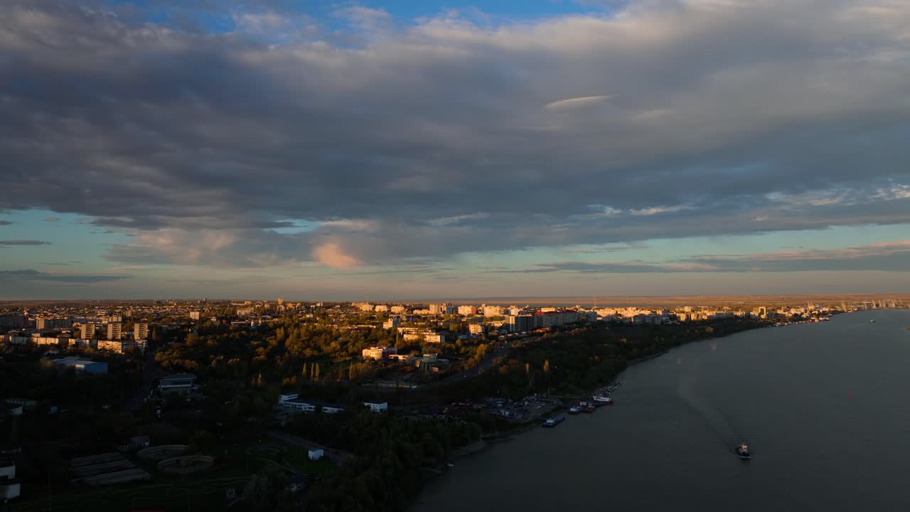 Aerial wide shot over big river revealing a city skyline blending seamlessly with the natural landscape in sunset warm light, 4K50Fps
