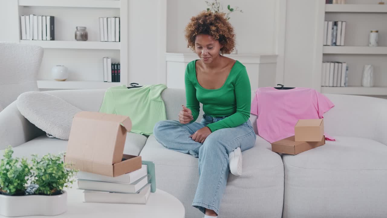 Young happy african american woman blogger records video sits on sofa with boxes