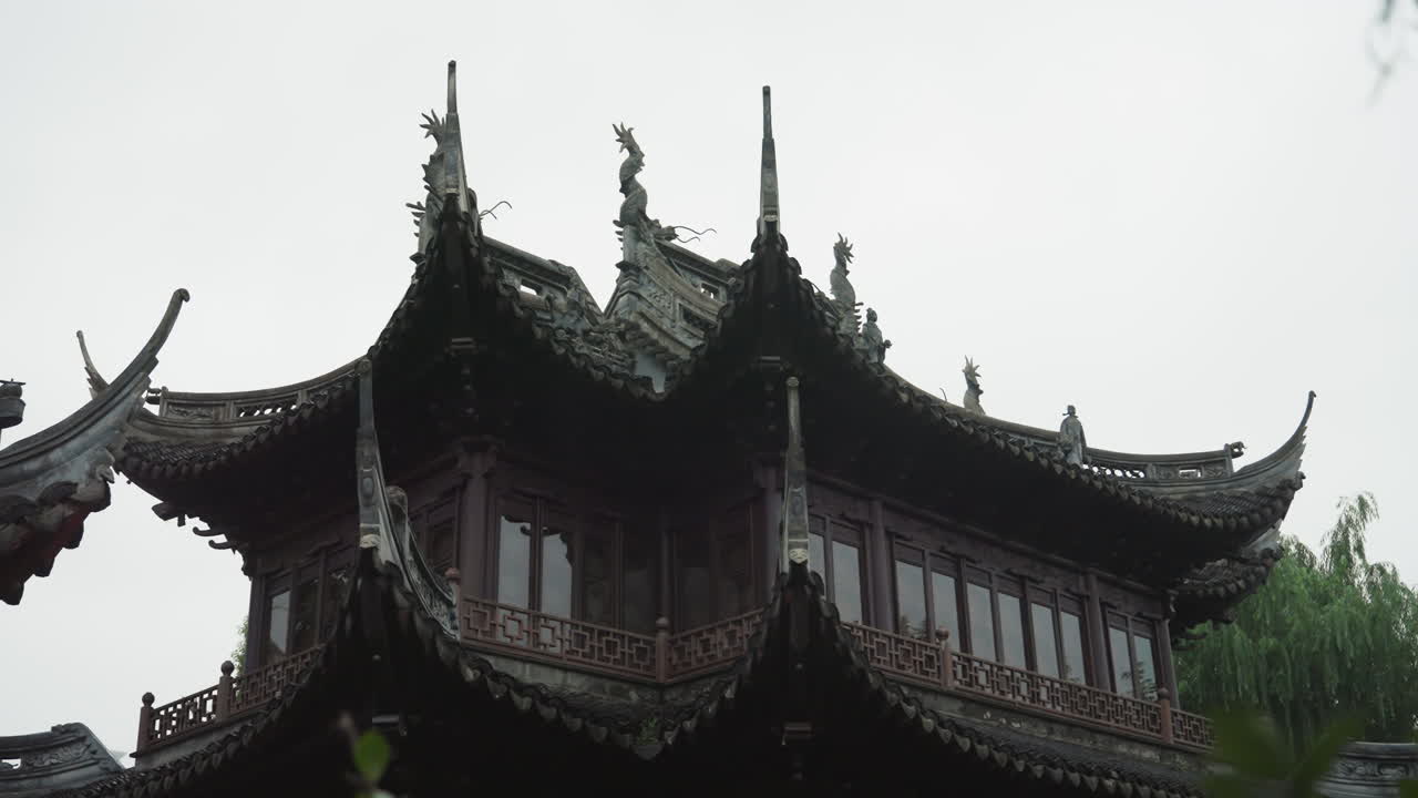 Kapalı gökyüzü altında yağmurlu pagoda çatısı, söğüt dallarıyla çerçevelenmiş süslü kavisli saçaklar ve katmanlı kiremitler, koyu ahşap oyma ve dekoratif braketler, kasvetli yumuşak ışık derin gölgeler düşürüyor, tarihi.