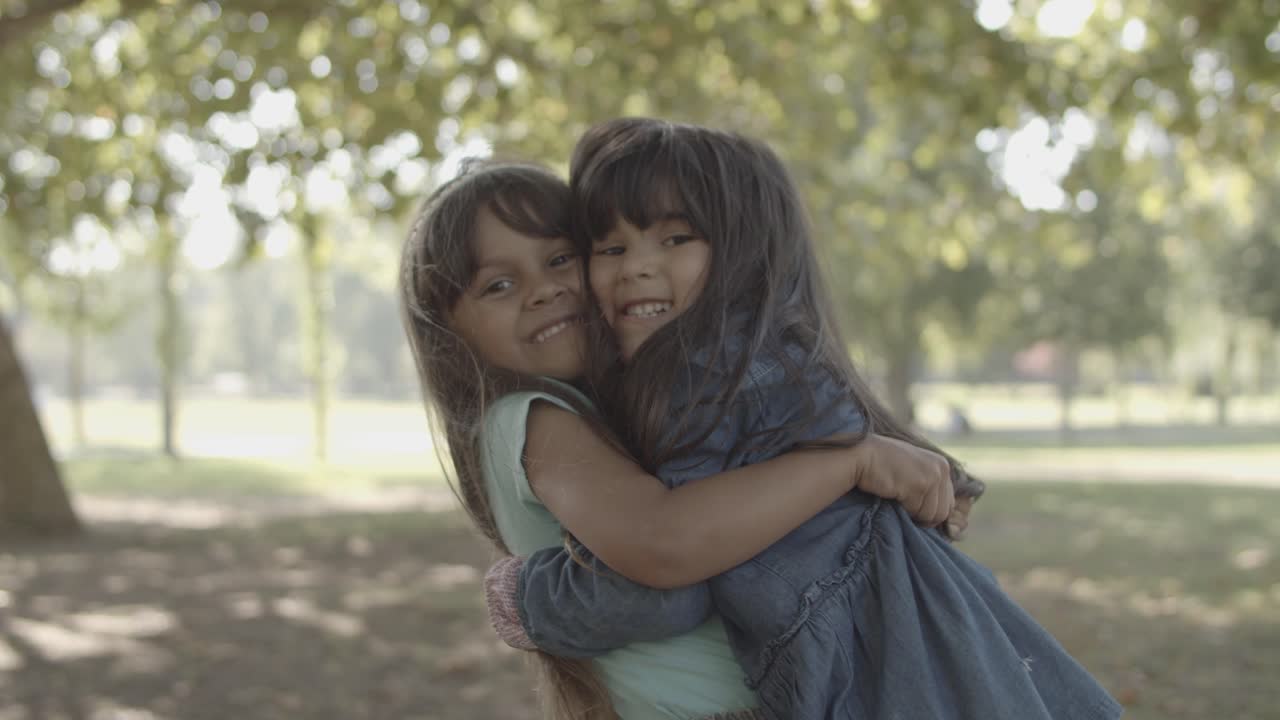 Menininhas latinas fofas se abraçando e sorrindo no parque.