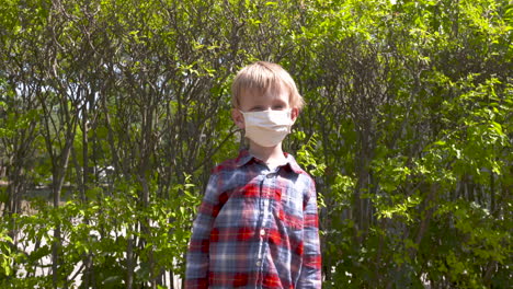 Portrait-of-a-cute-little-boy-standing-outside-wearing-a-face-mask