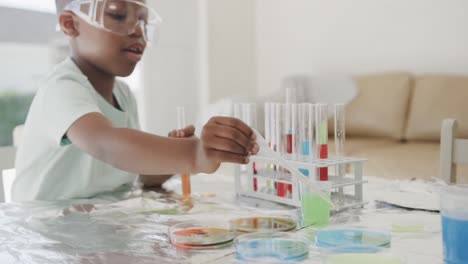 African-american-boy-sitting-at-table-holding-test-tubes-with-liquid,-in-slow-motion