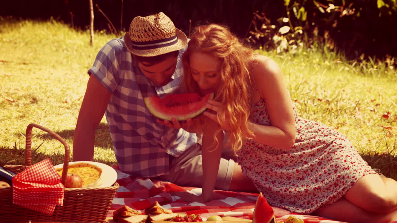 피크닉 을 하고 있는 젊은 부부 가 수박 을 먹고 있다