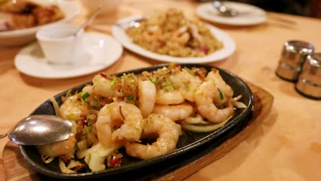 Close-up of a sizzling prawn entrée with vegetables and fried rice on a warmly lit restaurant table, shallow depth of field, slight camera pan