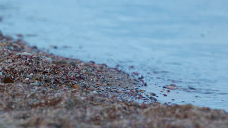 a close up view of calm ocean waves hitting small pebbles on the beach