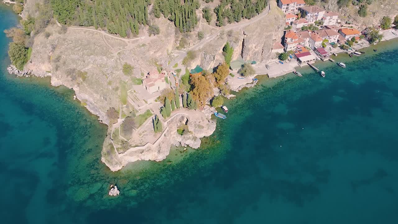 monasterio en el borde de las rocas sobre un lago prístino verde y azul disparado por un dron