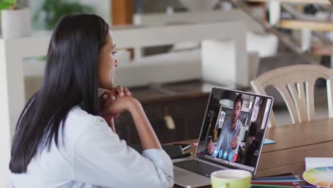 Mixed-race-businesswoman-sitting-at-table-using-laptop-having-video-call-with-male-colleague