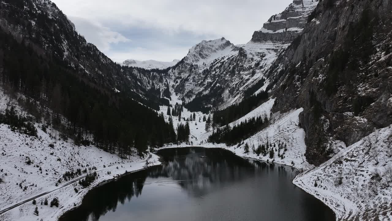 Una vista aerea svela la tranquillità del Tahlalpsee a Filzbach, Glarus Nord, Svizzera, dove cime montuose innevate incorniciano il lago sereno nella valle, con bellezza naturale e pace.
