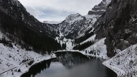 Aerial-view-unveils-the-tranquility-of-Tahlalpsee-in-Filzbach,-Glarus-Nord,-Switzerland,-where-snow-capped-mountain-peaks-frame-the-serene-lake-in-the-valley,-with-natural-beauty-and-peacefulness