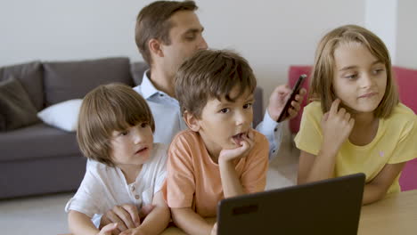 father sitting with cute children and using smartphone