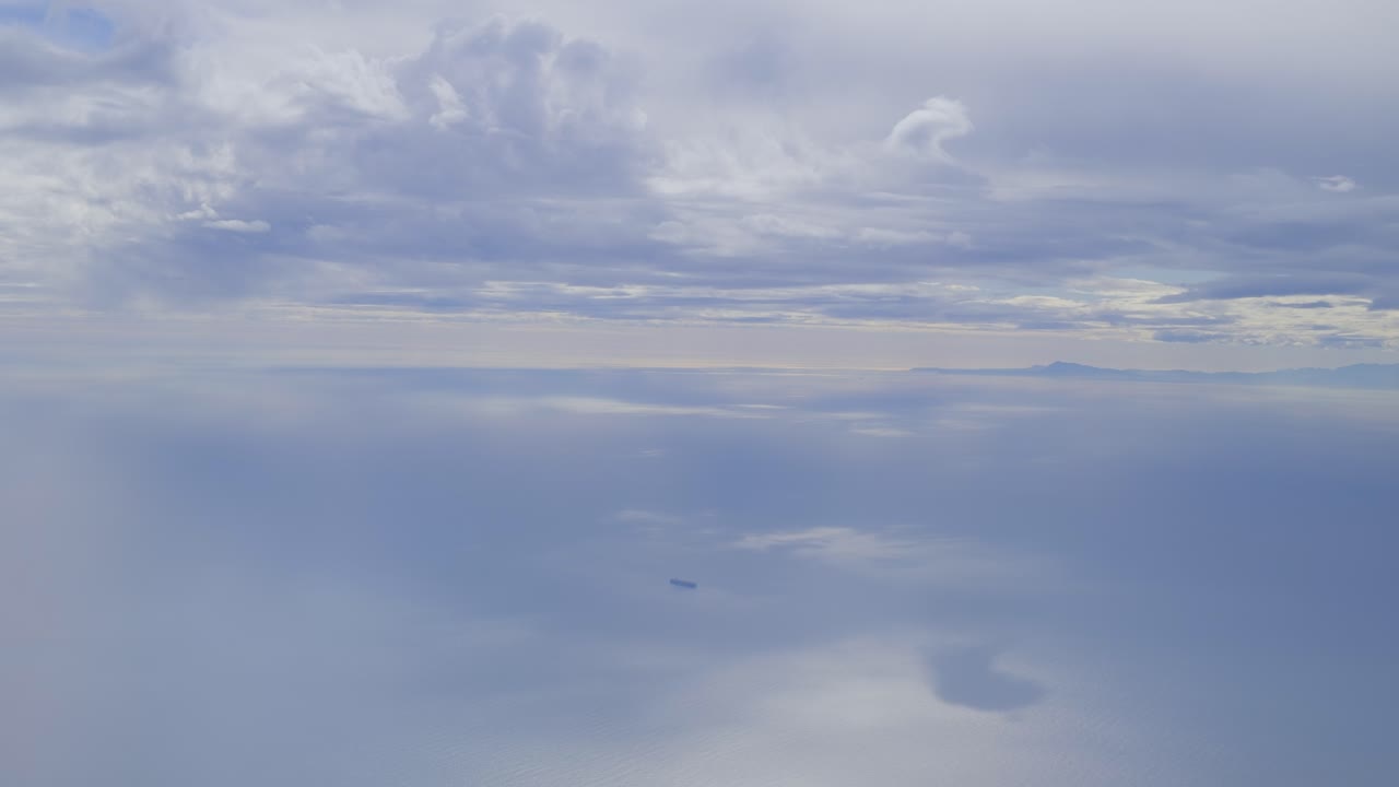 A vast serene ocean under a cloudy sky with a faint outline of distant land with cargo ship