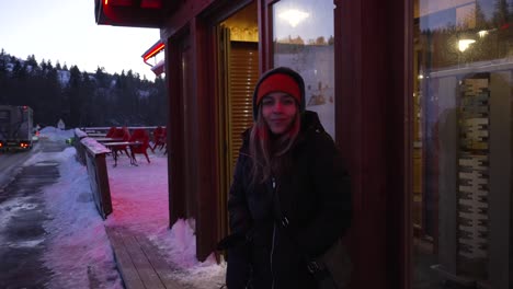 young blonde girl with cold expression, warmly dressed at the door of her ski resort