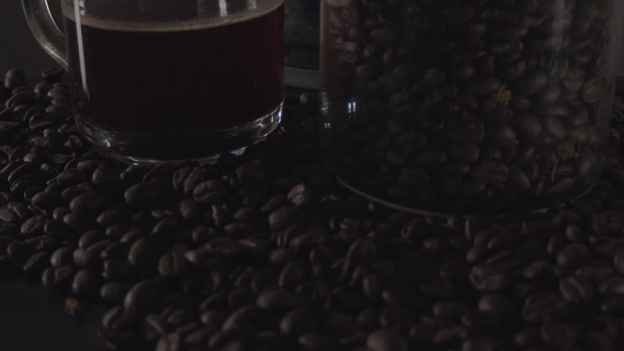 A close-up shot of coffee beans into a reveal of a glass cup and container.