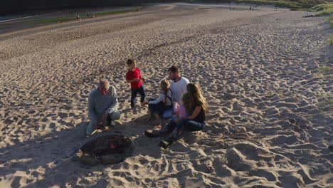 drone shot of multi-generation family having evening barbecue around fire on beach vacation