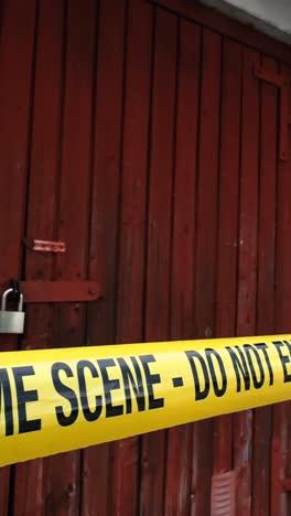 close up or closeup footage of a yellow colored vibrant crime scene do not enter tape in front of a wooden red or brown garage door that is locked showing that a crime has happened. cloudy day time